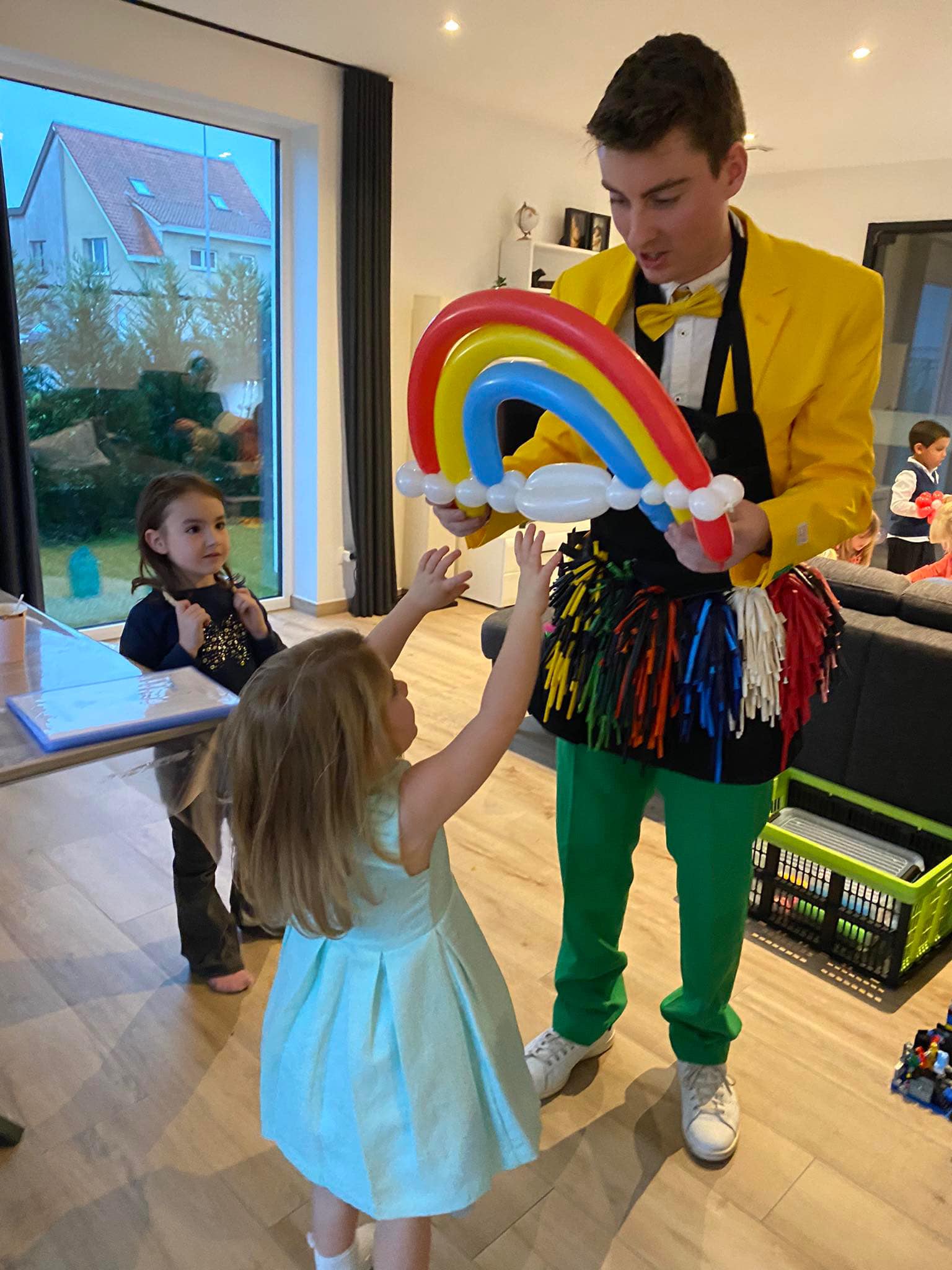 Een ballonplooier houdt een ballonregenboog vast terwijl een meisje er enthousiast naar reikt.