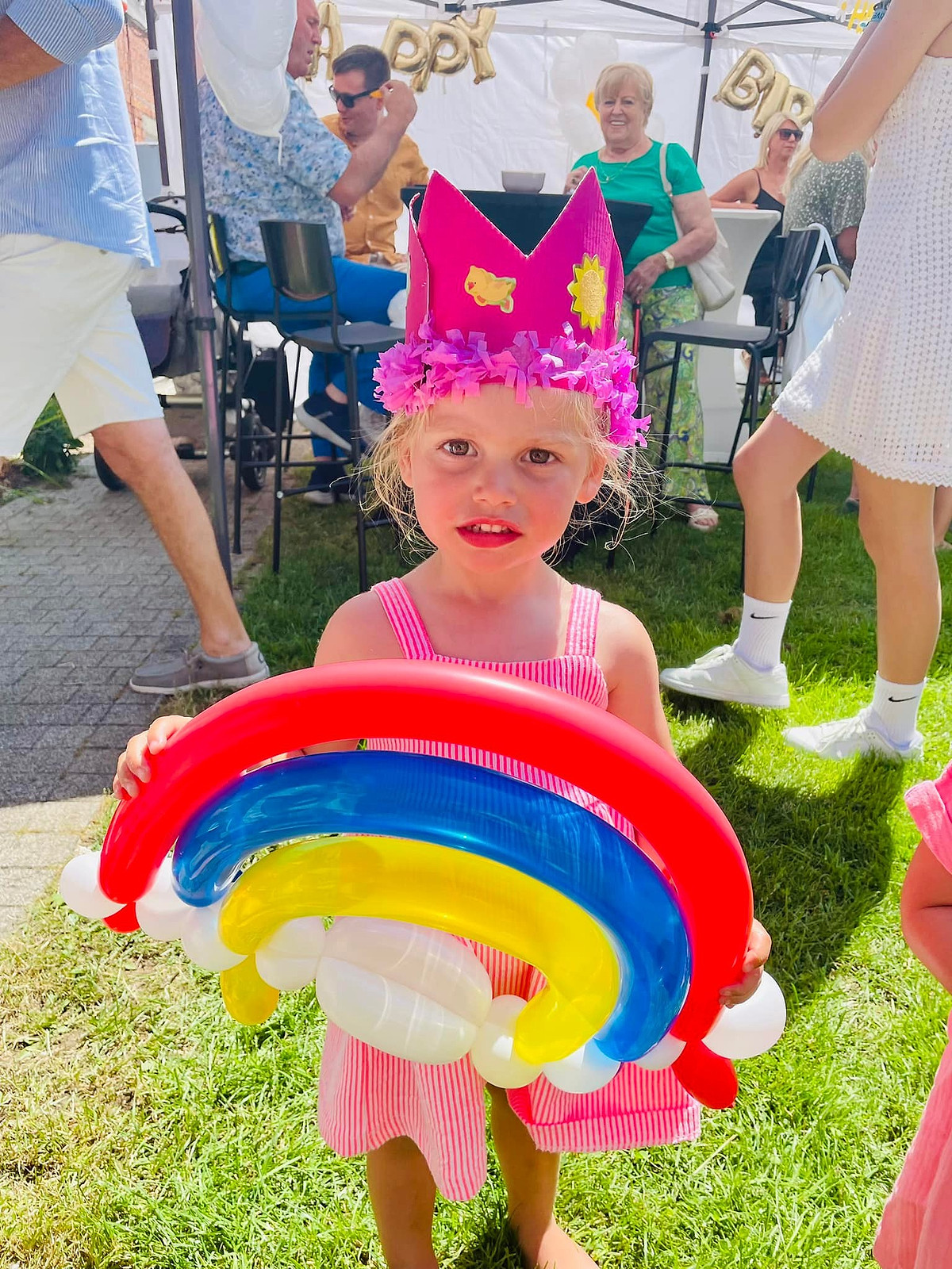 Een meisje met een roze kroon houdt een ballonregenboog vast.