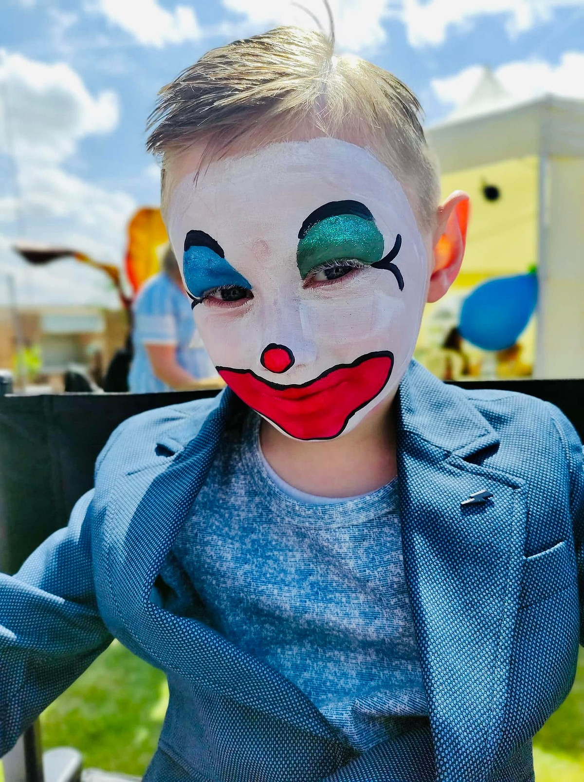 Een jongen met clowngrime: een wit gezicht, een rode neus en een grote rode mond.