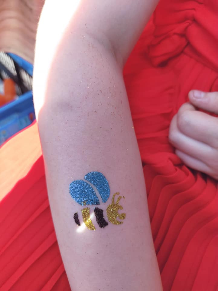 Een glittertattoo van een blauw-gele bij op een arm.