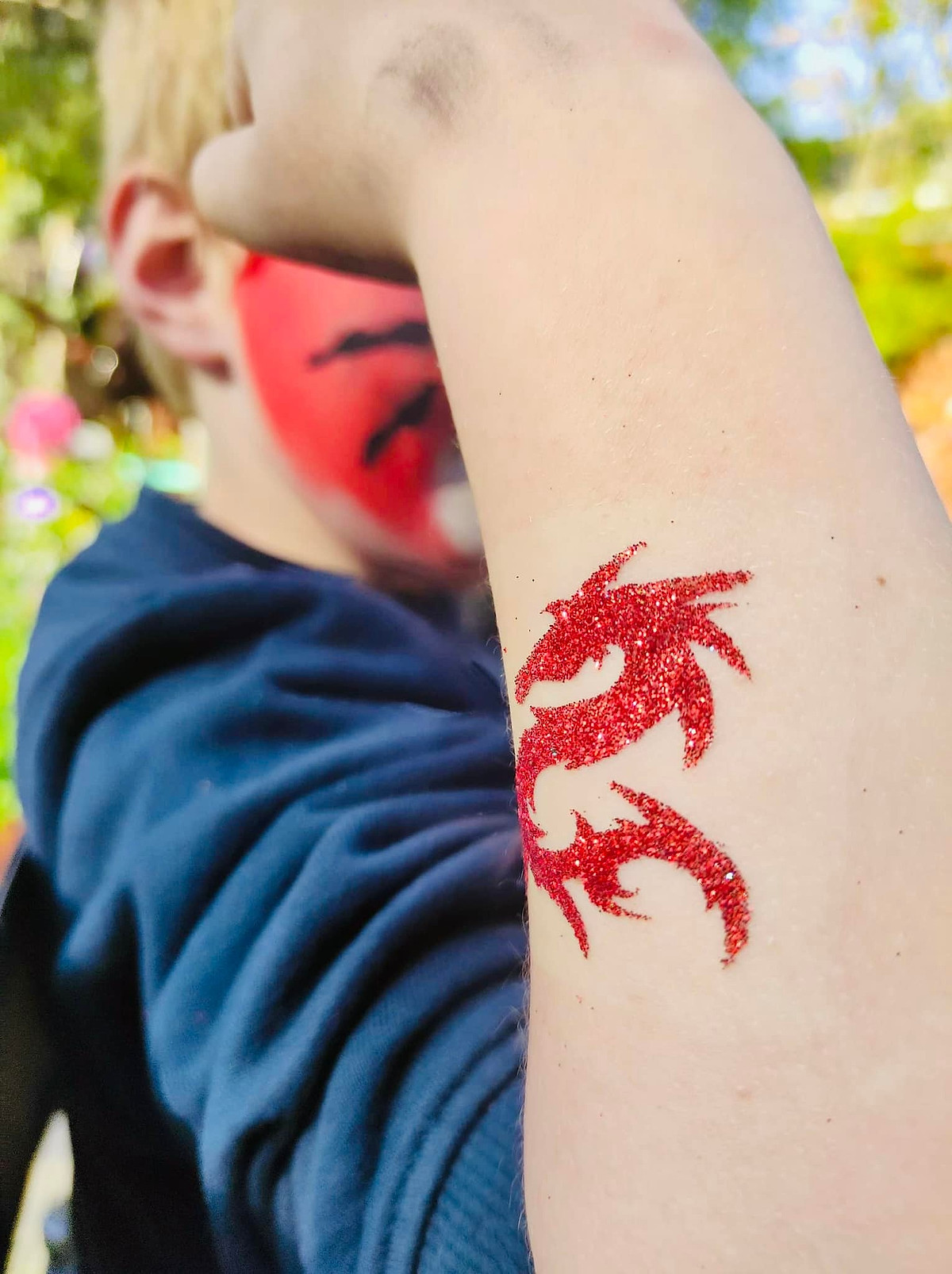 Een rode glittertattoo van een draak op de arm van een kind.