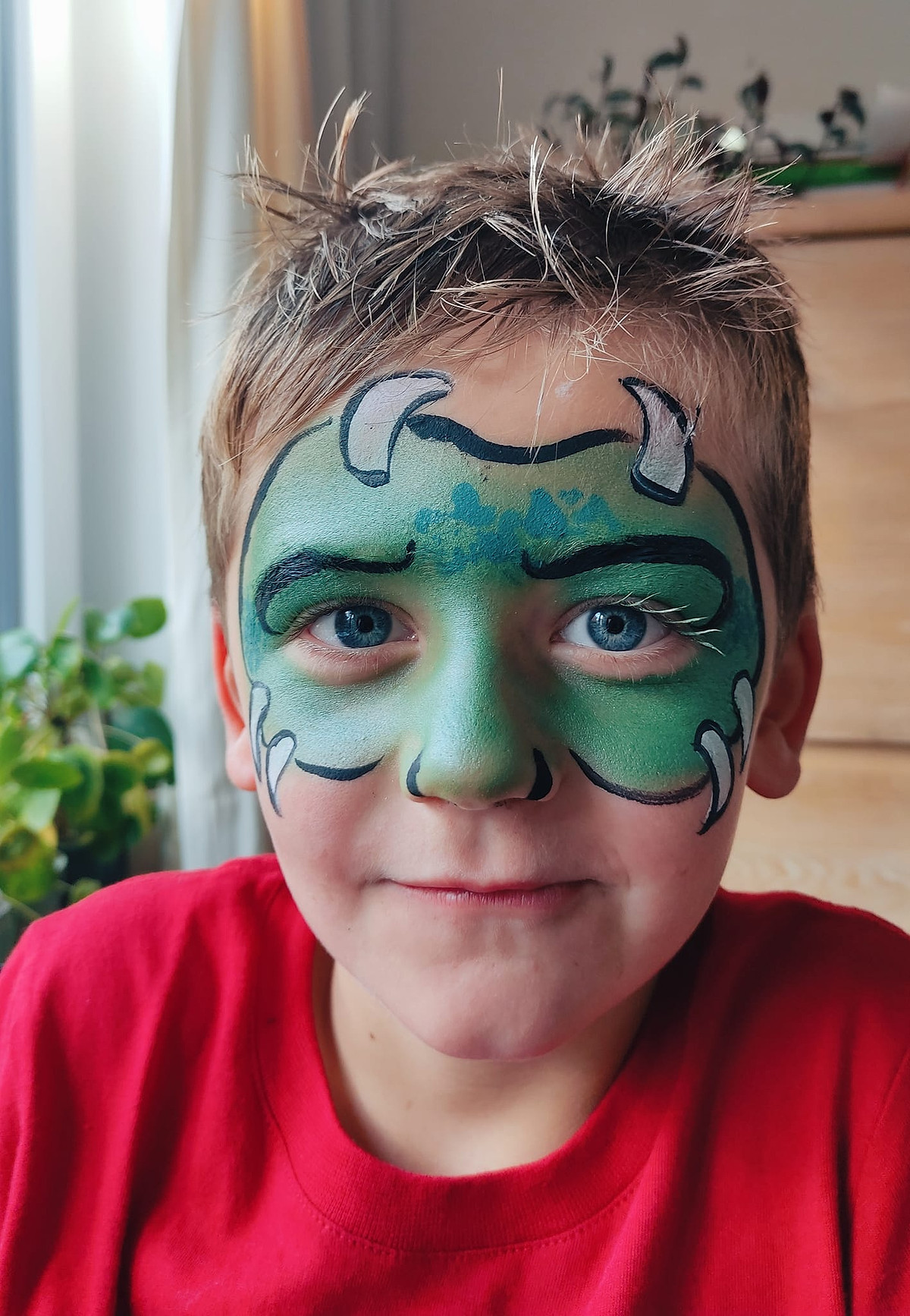 Een jongen met groene monstergrime en kleine hoorntjes op zijn voorhoofd.
