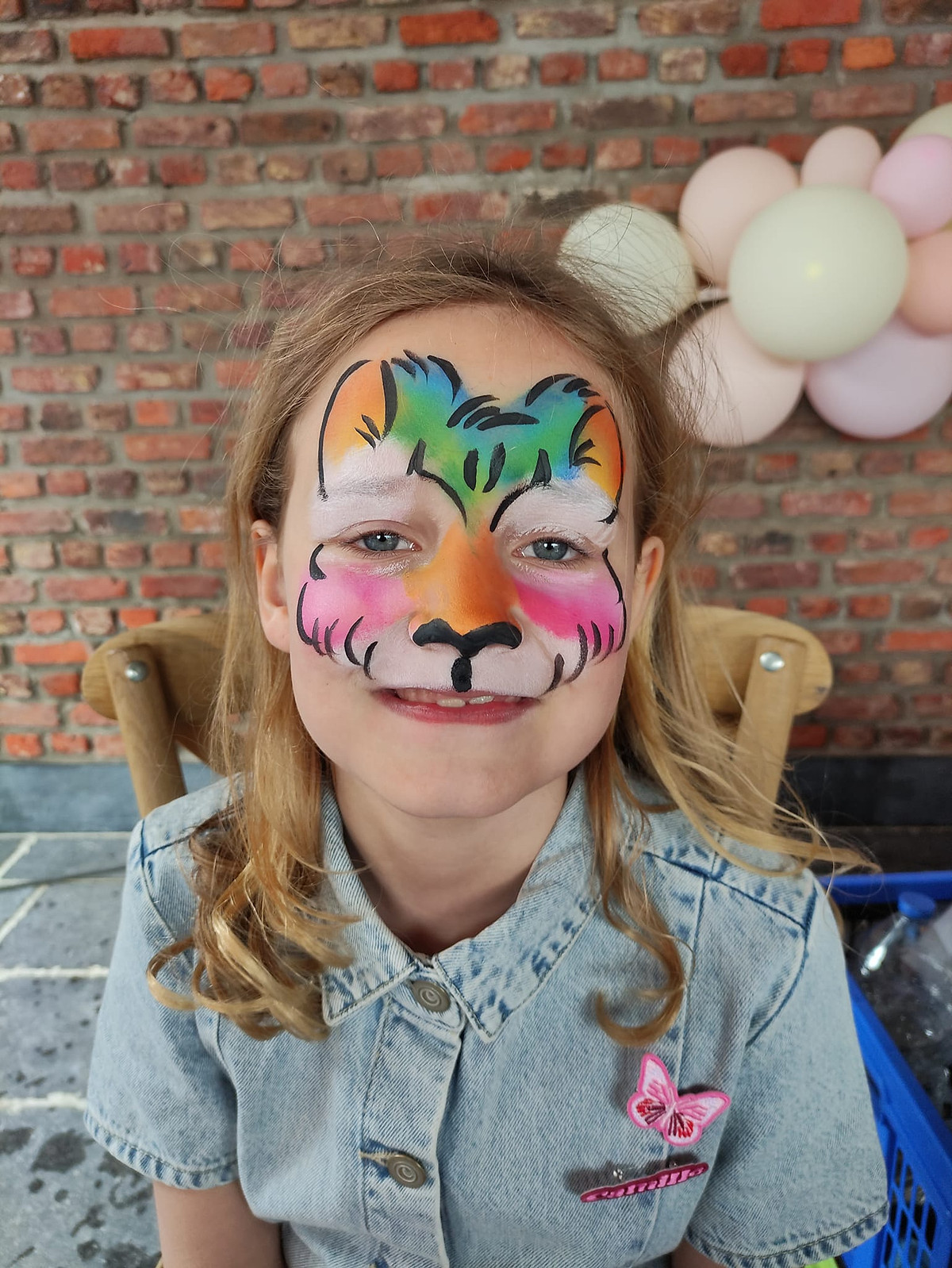 Een meisje met een kleurrijke tijger in groen, roze en oranje op haar gezicht.