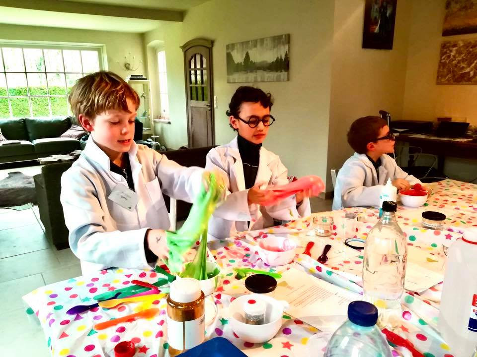 Kinderen in witte labojassen experimenteren aan tafel tijdens een laboratoriumfeest.