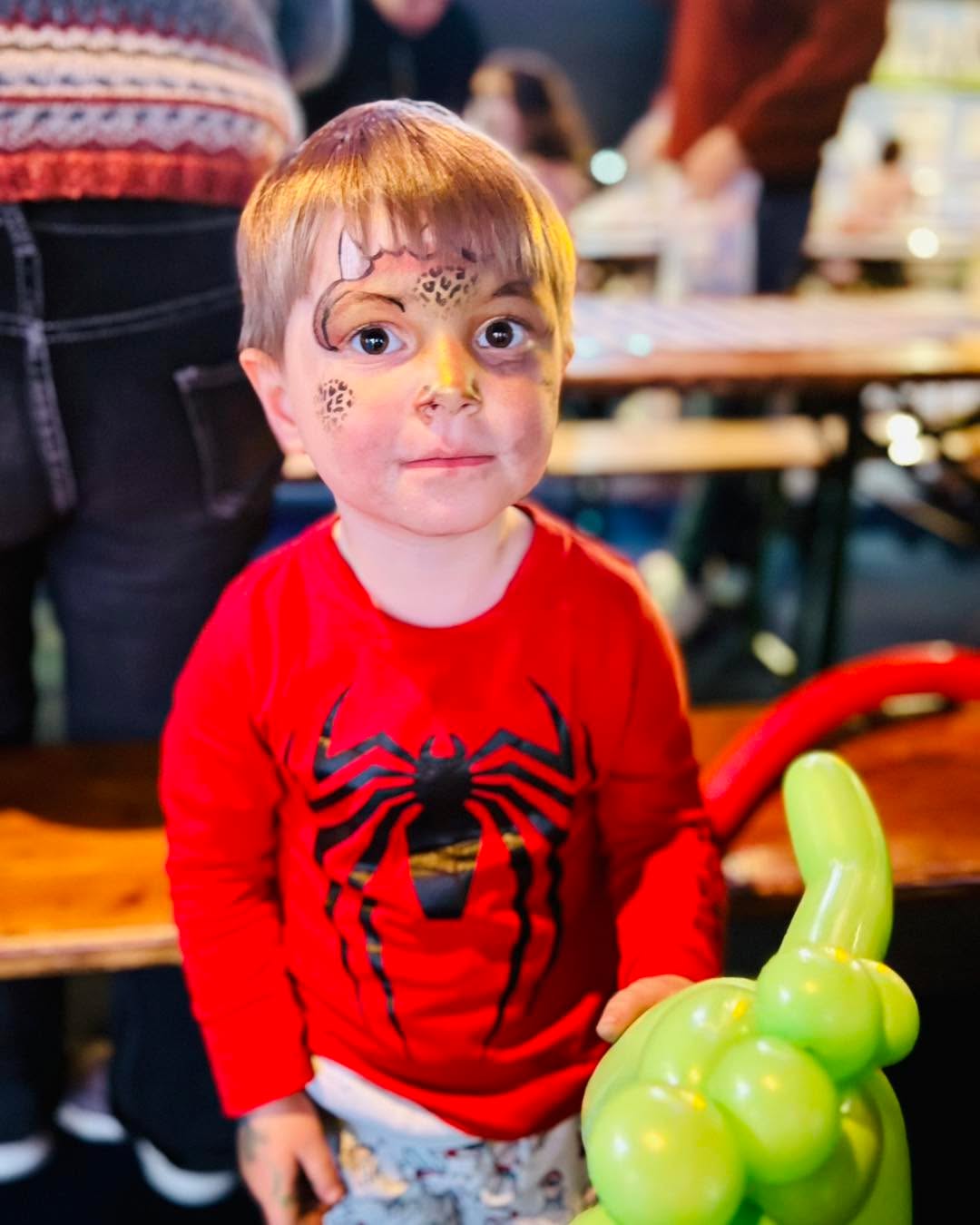 Een jongen met luipaardgrime rond zijn oog houdt een groen ballonfiguur vast.