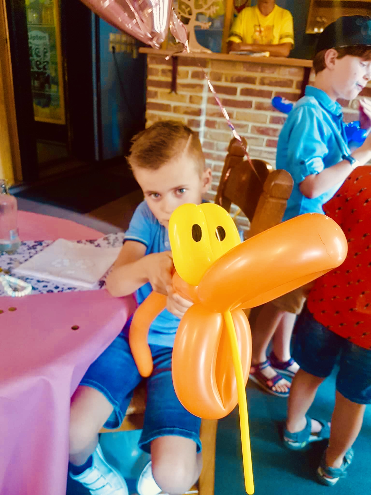 Een jongen toont een groot oranje ballonfiguur dat op een hond lijkt.