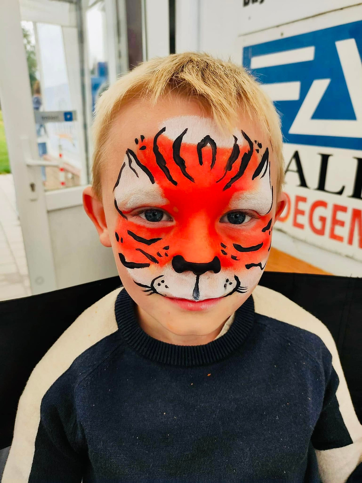 Een jongen met felle oranje tijgergrime met zwarte strepen.