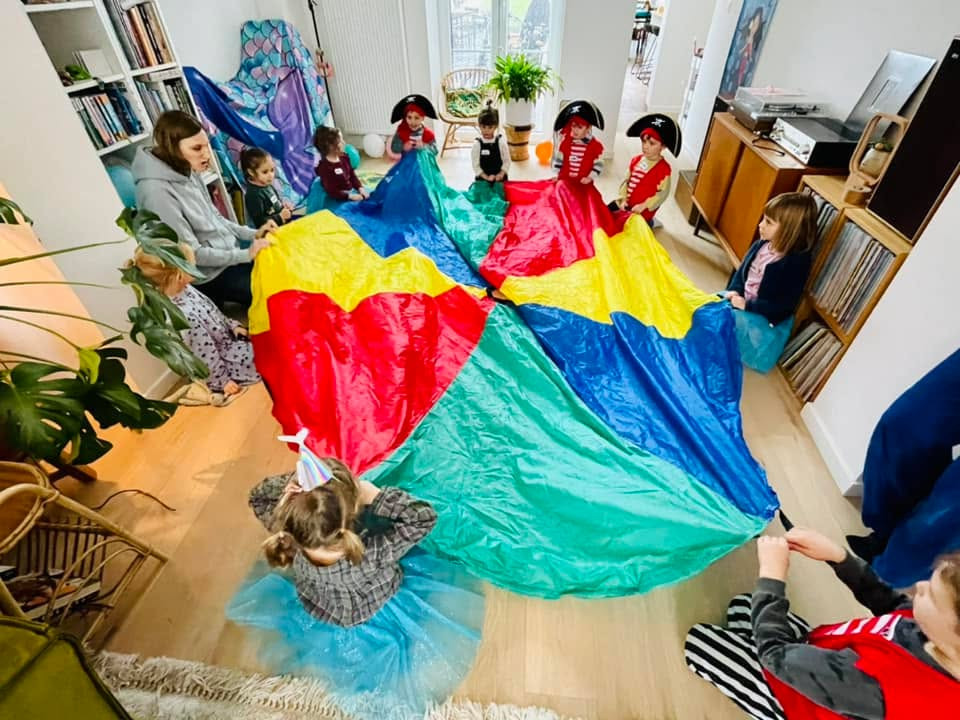 Kinderen spelen samen met een groot gekleurd parachutedoek.