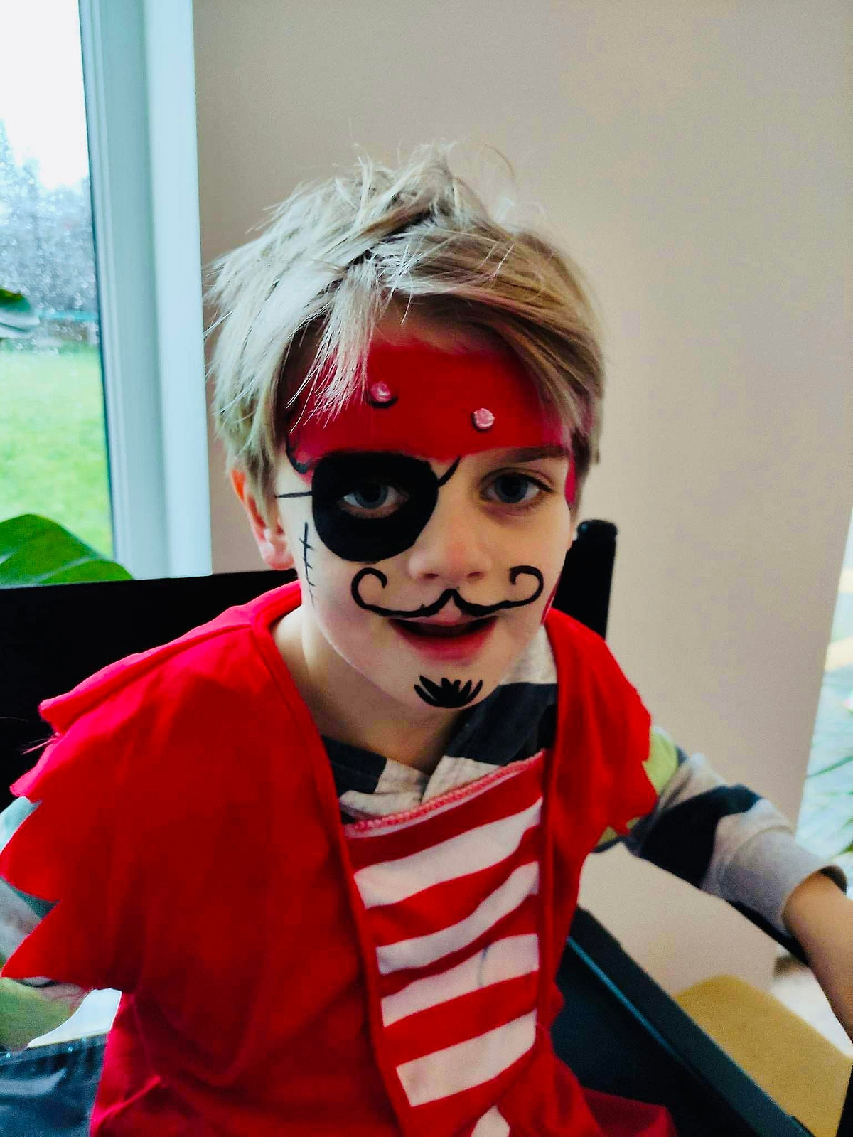 Een jongen met piratengrime, een ooglapje en een snor, in een rood-wit gestreepte trui.