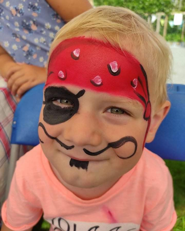 Een lachende jongen met piratengrime: een rode bandana, een ooglapje en een krulsnor.