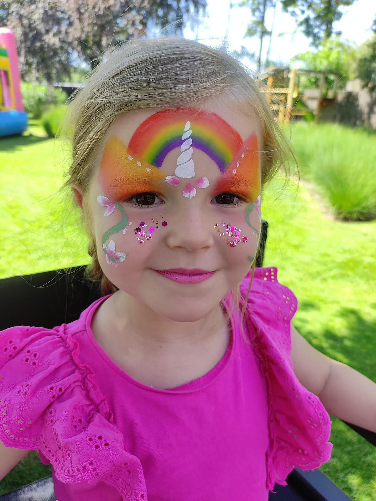 Een lachend meisje met een regenboog en een eenhoornhoorn op haar voorhoofd.