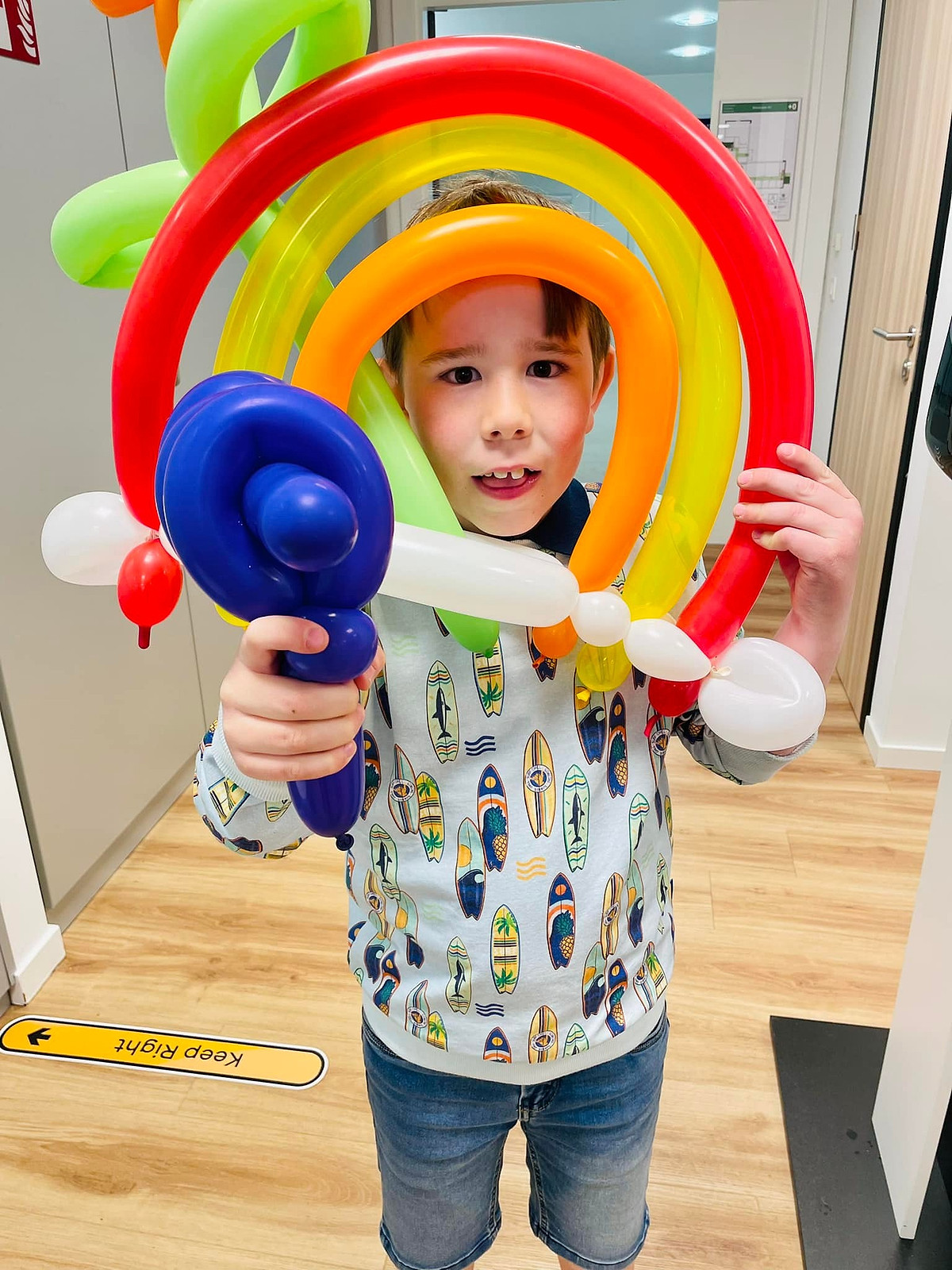 Een jongen houdt een ballonregenboog en een blauw ballonzwaard vast.