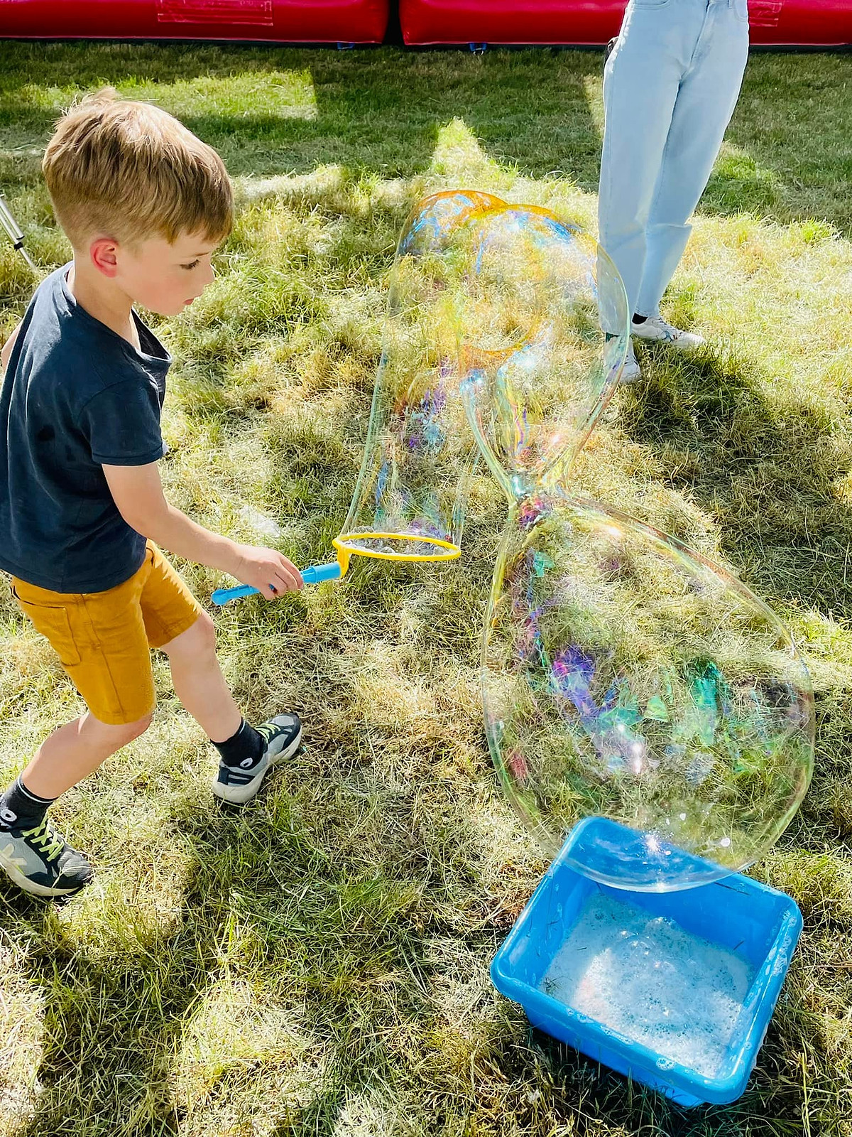 Een jongen maakt met een bellenstok een reuzezeepbel in het gras.