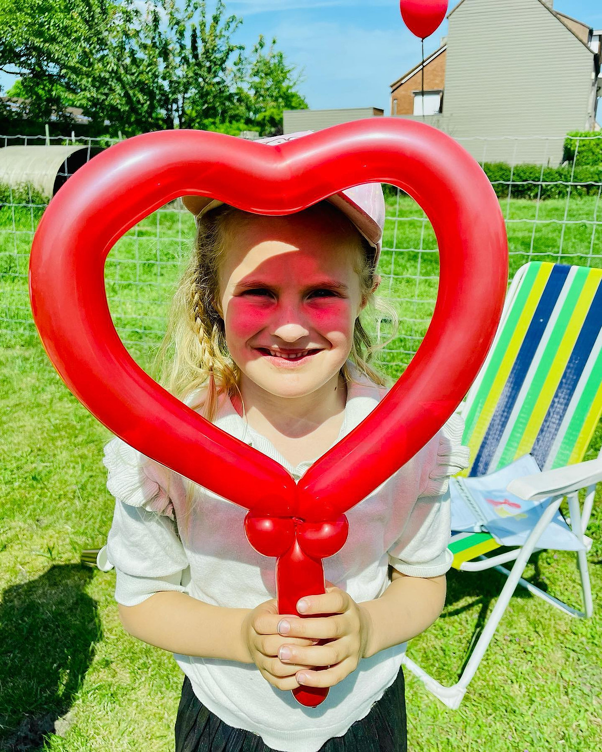 Een meisje kijkt lachend door een groot rood ballonhart.