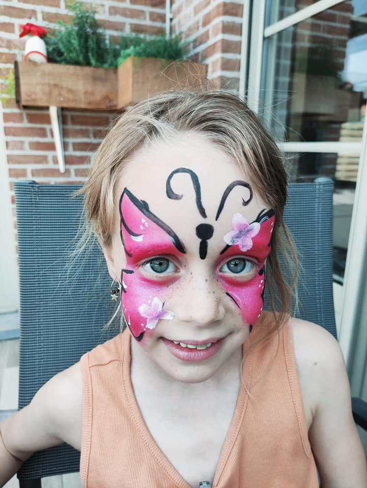 Een meisje lacht met roze vlindergrime rond haar ogen.