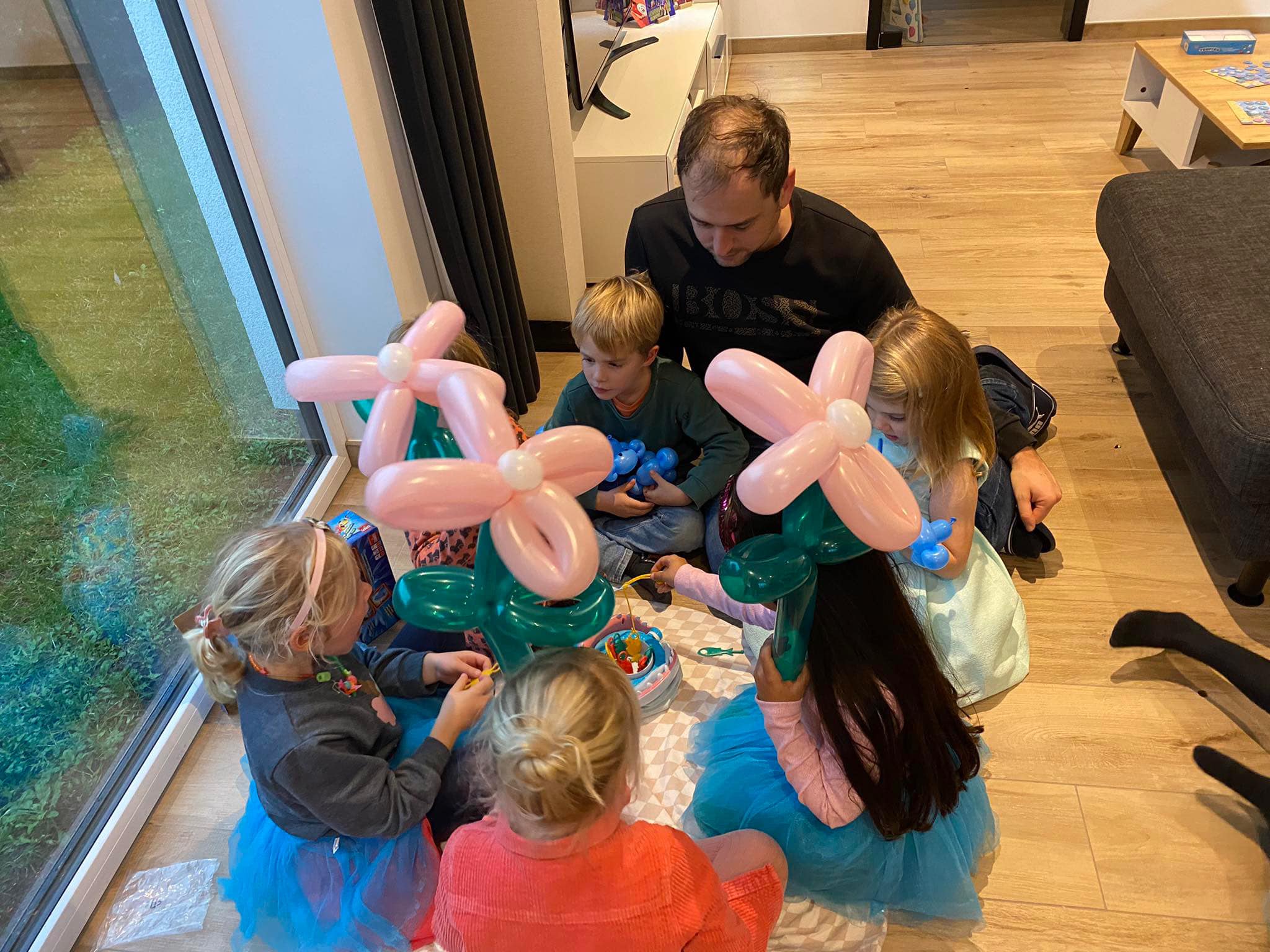Kinderen met roze ballonbloemen spelen samen een spelletje op de vloer.