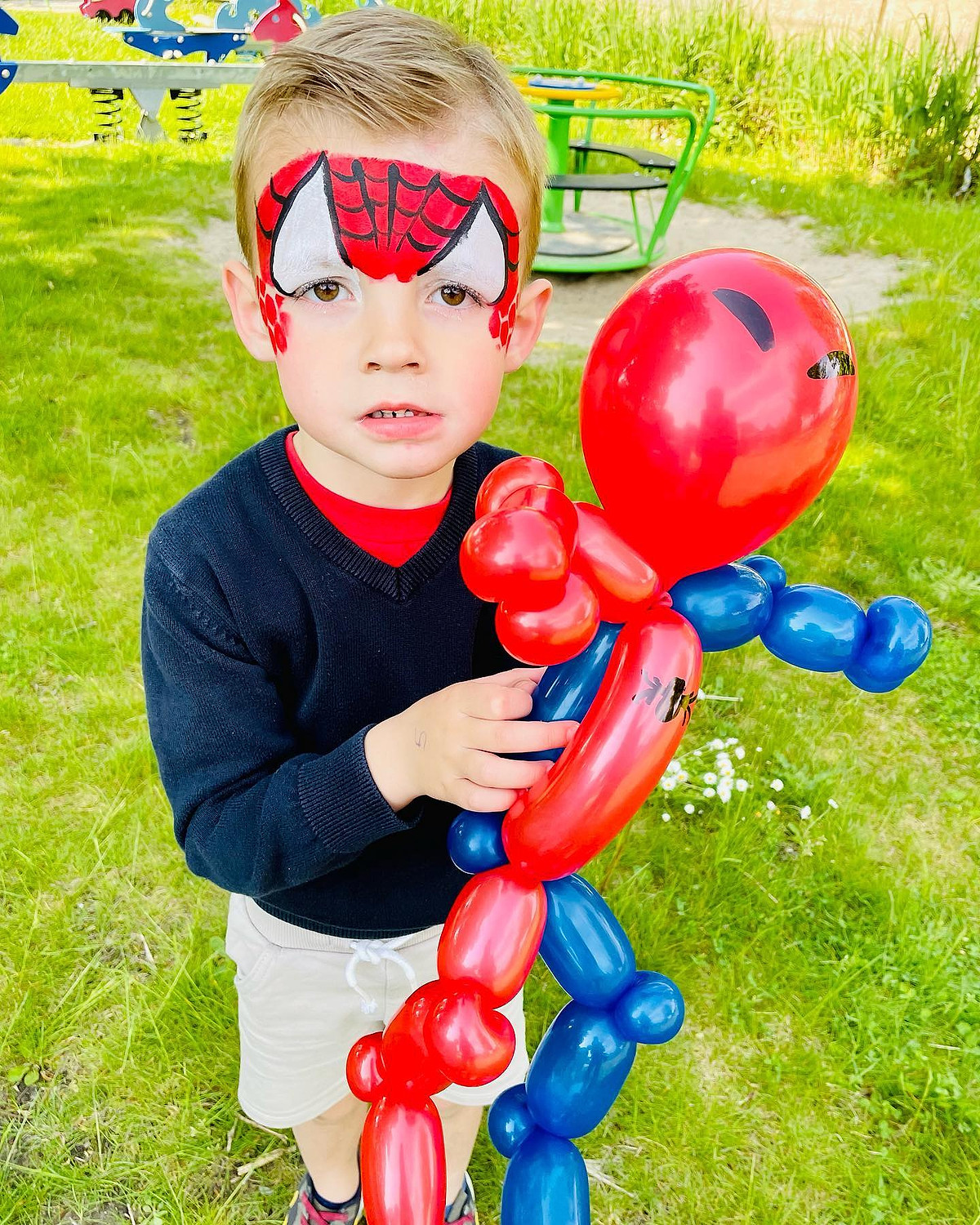 Een jongen met Spidermangrime houdt een rood-blauwe ballonspiderman vast.