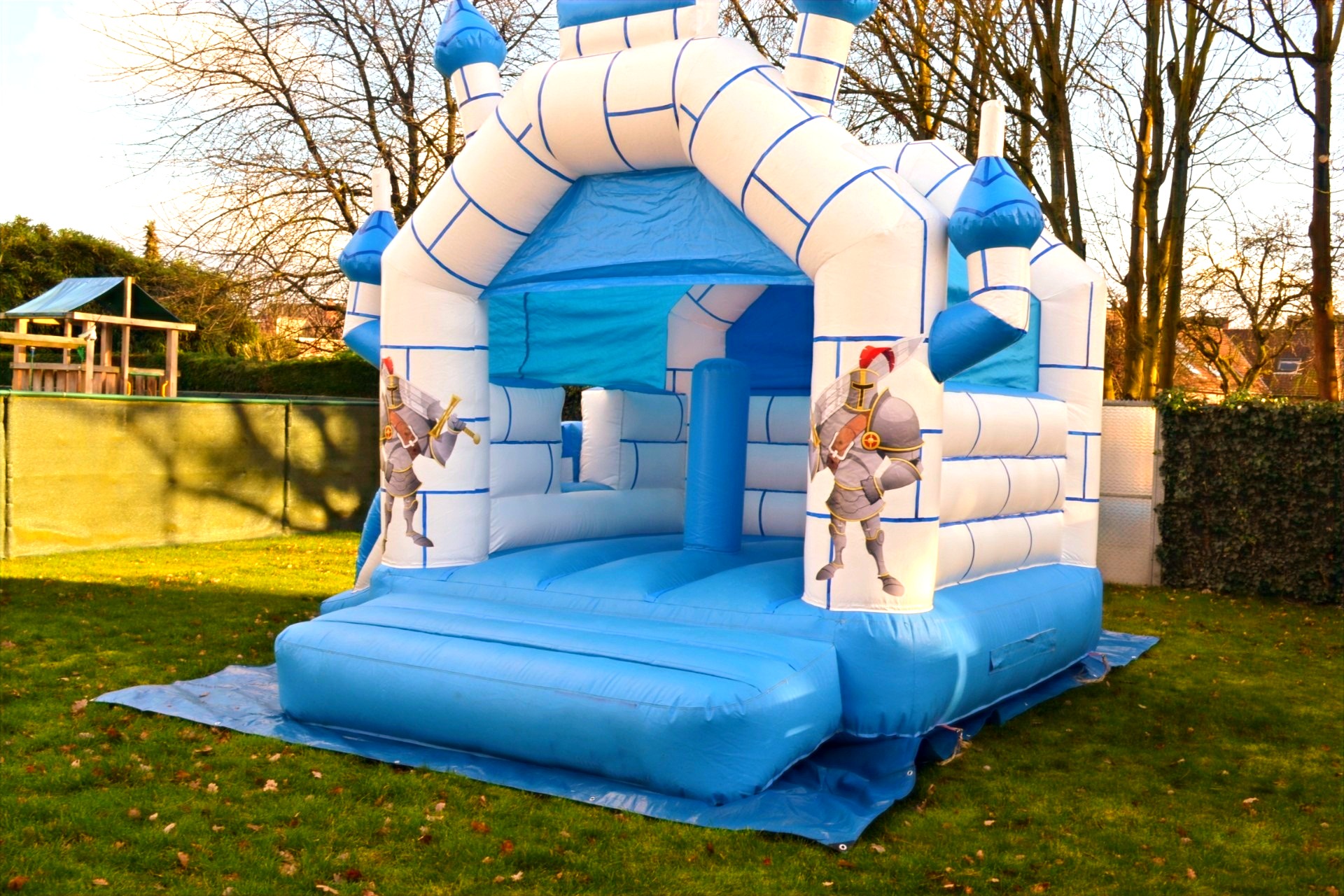Springkasteel Ridder schuin van achteren in een tuin, met een houten speeltuig op de achtergrond. Foto 5 van 8.