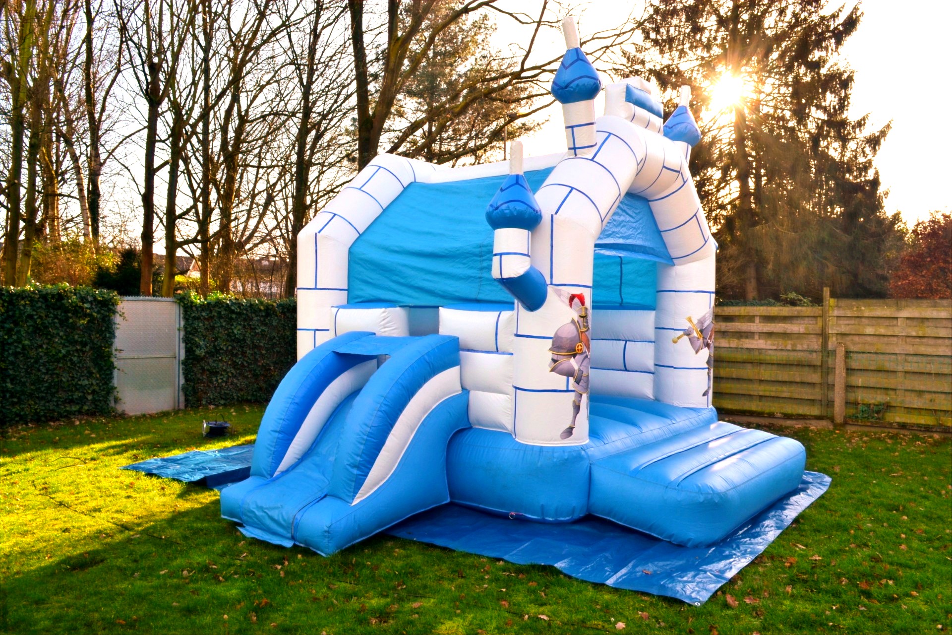 Springkasteel Ridder schuin van opzij, met de glijbaan links en de late zon achter de bomen. Foto 6 van 8.