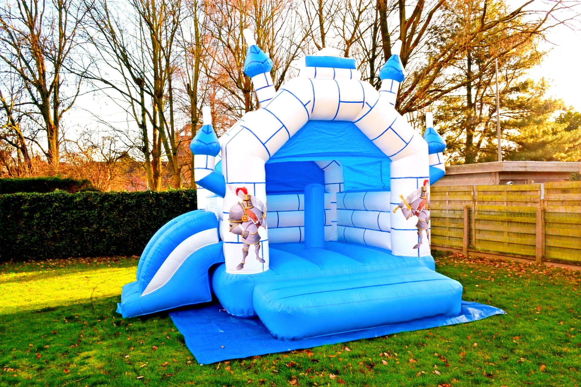Het blauw-witte springkasteel Ridder van vooraan gezien, op een grondzeil in het gras. Foto 7 van 8.