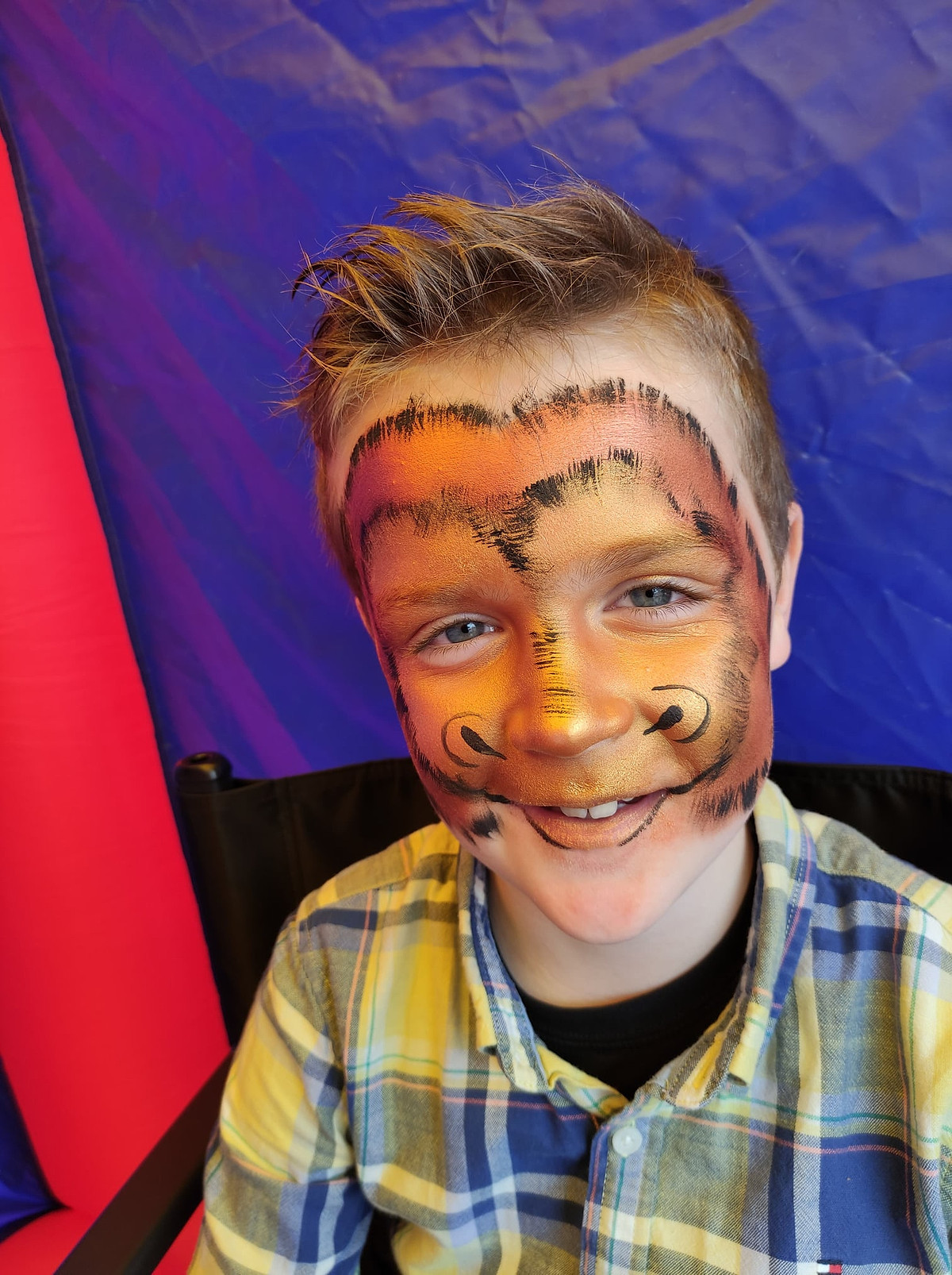 Een lachende jongen met tijgergrime over zijn hele gezicht.